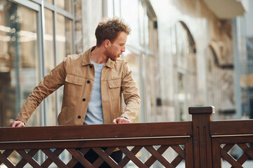 Canvas Print - Elegant young man in formal classy clothes leaning on wooden fence outdoors in the city