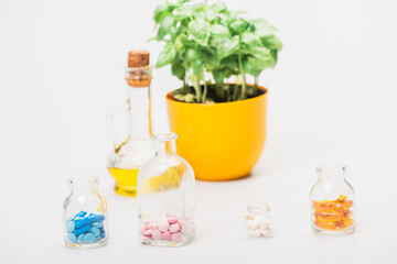 Wall Mural - selective focus of green plant in flowerpot near pills in glass bottles and essential oil on white background, naturopathy concept