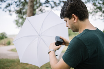 Canvas Print - Photographer setting flash light on a tripod with umbrella. Back of man preparing for photo session while setting flash to light stand with umbrella in nature.