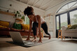 © StratfordProductions - Happy woman watching video on laptop while exercising on yoga mat at home - lock down workout