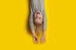 Surprised fair-haired boy hanging upside down with arms outstretched. Portrait of child on bright yellow background