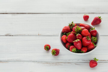 Fresh strawberries on ceramic bowl top view. Healthy food on white wooden table mockup. Delicious, sweet, juicy and ripe berry backgroung with copy space for text