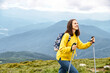 © Vadim Pastuh - A cheerful hiker girl in yellow sweater with a backpack walks with a sticks on mountains footpath with a scenic view on the background