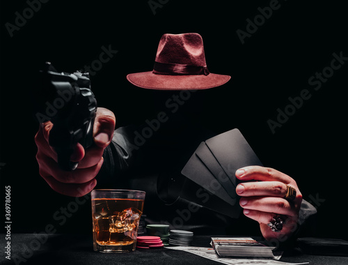 Gngster with gun and hat playing poker with cards.
