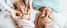 Two Girls Make Homemade Face And Hair Beauty Masks. Cucumbers For The Freshness Of The Skin Around The Eyes. Women Take Care Of Youthful Skin. Girlfriends Laugh At Home Lying On The Floor On Pillows.