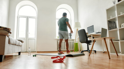 Wall Mural - Give up. Full length shot of young active man finishing exercising with resistance band during morning workout at home. Sport, healthy lifestyle