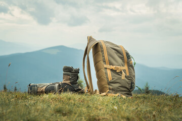 Khaki color boots and backpack standing on a grass on top of a mountain hill.