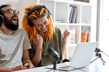 Laughing out loud. Couple of bloggers, young man and woman in headphones watching something on laptop and laughing while recording reaction video blog or vlog