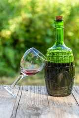 Glass bottle with red wine and a glass. on fresh air. Against the background of nature.