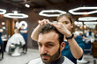 © Svitlana - Close up portrait of young handsome bearded man visiting barbershop. Professional barber girl making new trendy haircut for a client