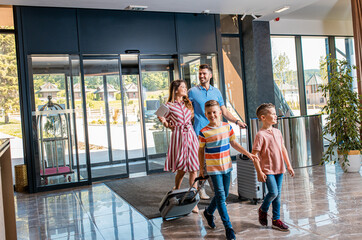Wall Mural - smiling family of four enters to the hotel lobby to check in at the reception for vacation.