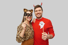 Holiday, Photo Booth And People Concept - Happy Smiling Couple In Halloween Costumes Of Devil And Leopard With Party Accessories Over Grey Background