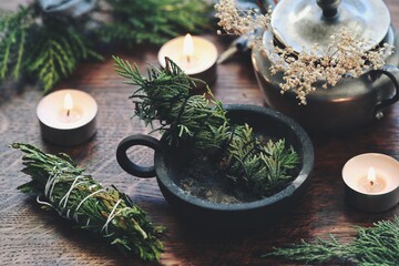 Cedar hand made smoke cleansing stick in cast iron ash holder burner on a wiccan witch altar. Cedar bundles for energy cleansing, alternative to sage smudge. Evergreens, fir, candles in background