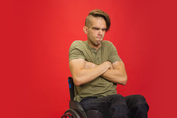 Wall Mural - Offended. Caucasian young disabled man's portrait isolated on red studio background. Beautiful male model in casual style. Concept of human emotions, facial expression, sales, ad, inclusion. Copyspace