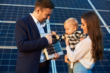 Wall Mural - Close-up shot of young family getting acquainted with alternative sources of energy, father holding small pv module showing to baby boy