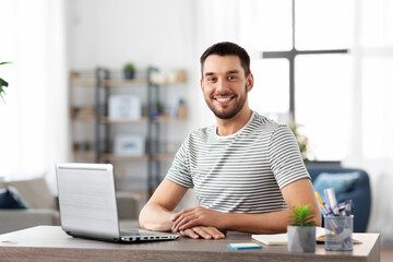 technology, remote job and business concept - happy smiling man with laptop computer working at home office