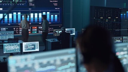 Poster - Two Software Engineers Talking Next to a Big Screen in a Modern Monitoring Office with Live Analysis Feed with Charts. Monitoring Room Big Data Scientists and Managers Sit in Front of Computers.