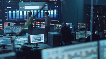 Fototapete - Two Software Engineers Talking Next to a Big Screen in a Modern Monitoring Office with Live Analysis Feed with Charts. Monitoring Room Big Data Scientists and Managers Sit in Front of Computers.