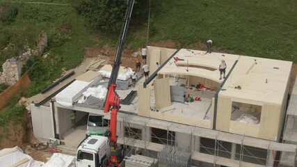 Wall Mural - DRONE: Group of men works on a cross-laminated timber house under construction. Truck boom lift towers above a modern massive wood house being built in the countryside. Construction workers on the job