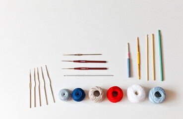 Different types of crochet hooks and balls of multicolored cotton yarn on a white background. Needlework and hobby concept. Place for text, flat lay, close-up, copy space, top view