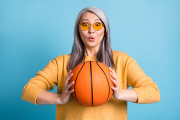 Don't miss basket. Photo of adorable attractive senior lady hold game ball excited look ready teach grandson play basketball active weekend wear yellow jumper bright blue color background