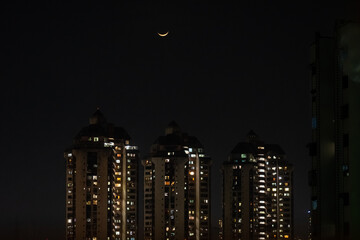 Crescent moon in night sky above skyscrapers in the city of Mumbai.