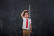Little kid boy measuring himself. School boy measuring his growth in height against a blackboard scale. Back to school. Pupil in uniform