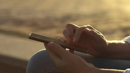 close-up young business woman using smartphone at sunset, female hands typing smartphone keyboard