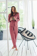 © standret - Cheerful young woman in pajamas standing indoors at daytime with cup of drink in hands