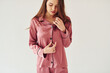© standret - Cheerful young woman in pajamas standing indoors against white background in the studio