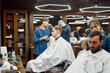 © Svitlana - People in barbershop. Young professional barber girl, female hairdresser working with hair clipper, serving young handsome guy sitting in barber shop chair