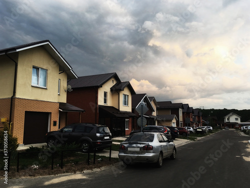 An empty street in the village. People stay home because of coronavirus (COVID 19) outbreak. Self-isolation (quarantine) in Moscow region, Russia. Brick houses, cottages, cars close-up. Dramatic sky