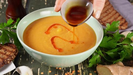 Wall Mural - Pouring a red oil on the top of lentil cream soup in a plate