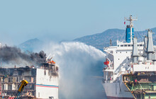 Burning Ship And Fire Fighting Boat Sprays Jets Of Water