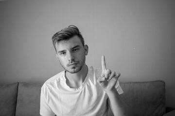 Black and White, Young man wearing a t-shirt with counting hand signs sitting in a isolated green background, showing number one