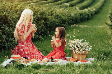 Young Mom with her Little Daughter Dressed Alike in Red Polka Dot Dress, Having Fun Time on a Picnic in the Field, Motherhood and Childhood Concept