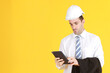 © cocorattanakorn - Handsome and smart engineer in suit and white shirt and Wearing a white safety engineer hat with hand holding smartphone isolated on yellow background. Copy Space