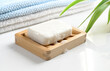 White Soap bar with foam on wooden soap dish and cotton towels on white table.