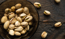 Pistachios In A Small Plate With Scattered Nuts Of Almonds Around A Plate On A Vintage Wooden Table As A Background. Pistachio Is A Healthy Vegetarian Protein Nutritious Food. Natural Nuts Snacks.