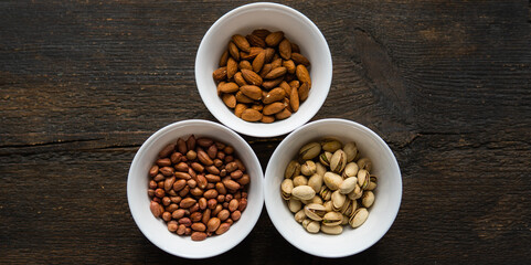 Wall Mural - Pistachio, peanut and almond in a small plates which standing on a black table. Nuts is a healthy vegetarian protein and nutritious food.