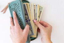 Buying For Dollars. A Woman's Hand Holds A Green Wallet And Counts Out Money. White Background