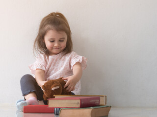 cute little girl smiling while playing with brown teddy bear. girl sitting next to pile of thick boo