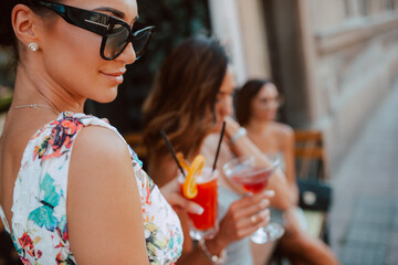 Three beautiful young caucasian women in short summer dresses are sitting and drinking cocktails in the cafe garden. Girls at parties