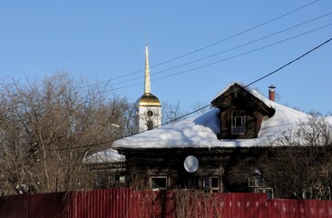 Ramenskoe. Moscow region. Russia. March 09. 2018. An old abandoned house and the bell tower of an Orthodox Church on a Sunny winter day.