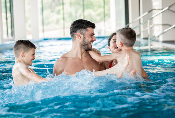 Wall Mural - smiling family of four having fun and relaxing in indoor swimming pool at hotel resort.