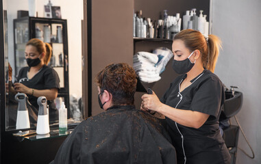 Hairdresser with protective masks cutting hair of woman