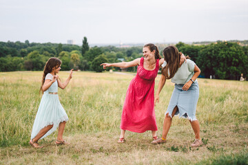 Three sister girls playing on the park outdoor. 3 girls, sisters, girlfriends in the field. Happy mother with younger and older daughter, two children plays in the meadow in summer in dresses