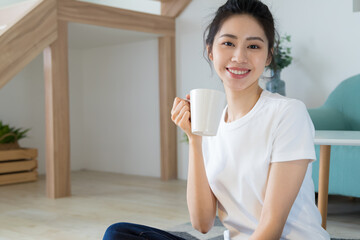 Wall Mural - Young asia woman with ponytail in white t-shirt holding a cup of coffee or tea relaxing at home in the morning.