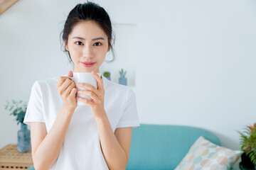 Young asia woman with ponytail in white t-shirt holding a cup of coffee or tea relaxing at home in the morning.