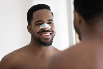 close up head shot smiling african american man with anti blackhead mask on nose looking in mirror a